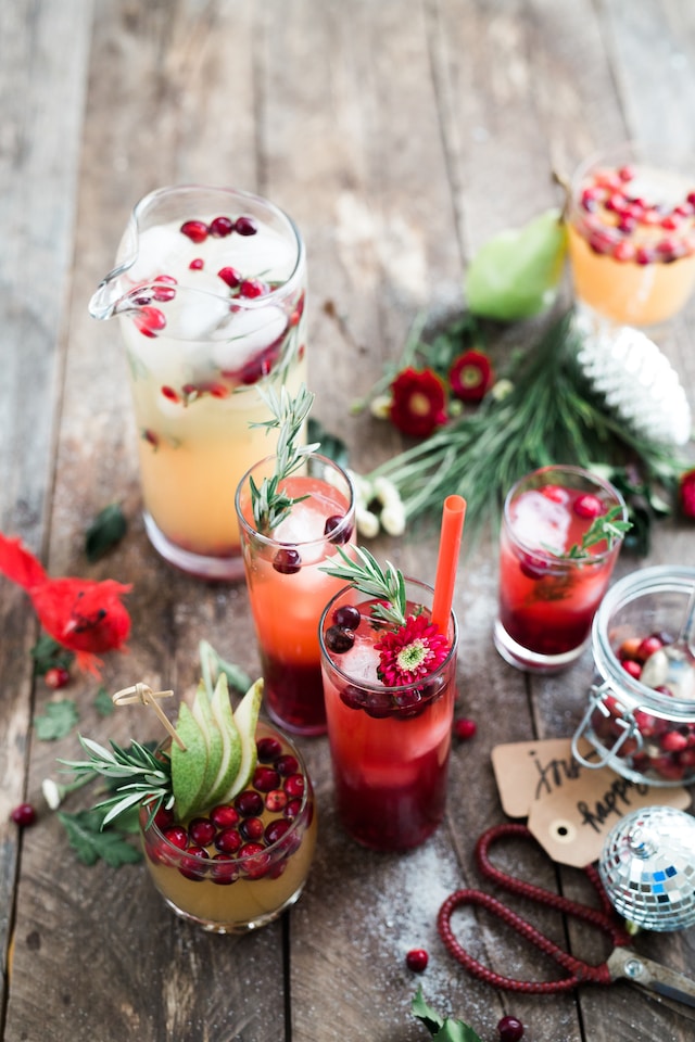 An assortment of holiday-themed fruit-based cocktails garnished with various fruits and herbs