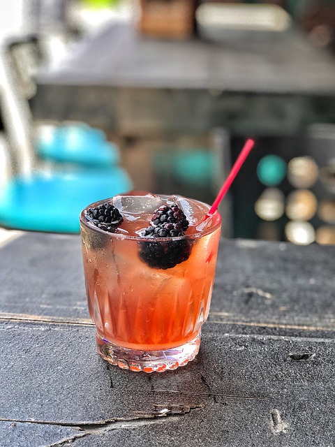 A reddish-hued drink in a clear glass with ice cubes and blackberry 