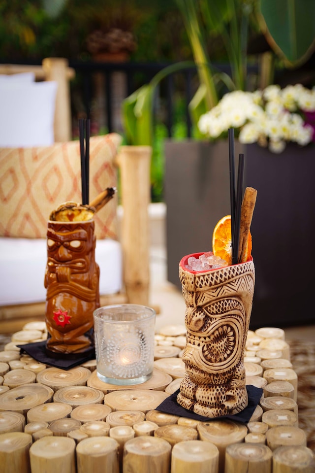 Quirky tiki mugs filled with cocktail mixes and an empty drinking glass in between.