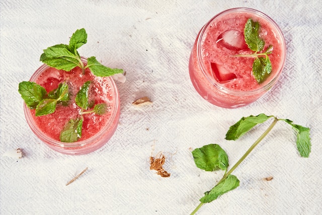Two glasses containing pink-colored liquid with a few ice cubes garnished with mint leaves