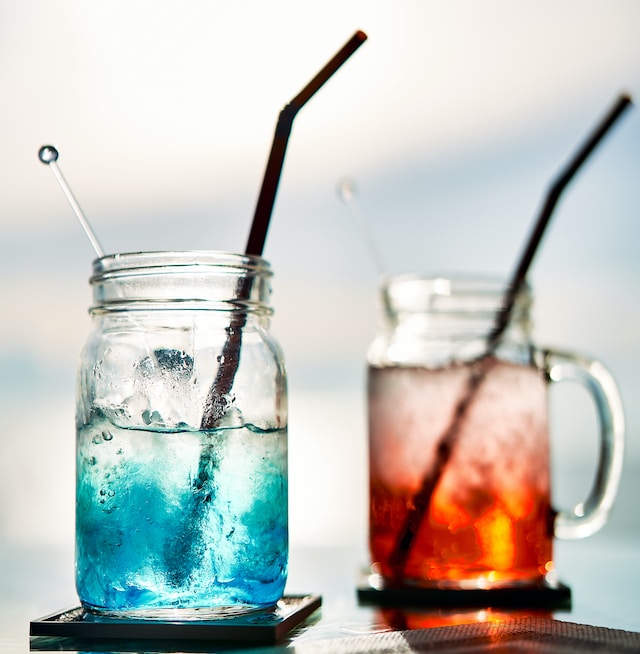 Two clear glasses with straws containing blue and red-colored drinks