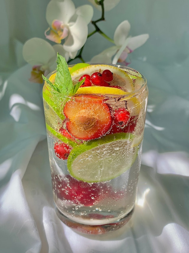 A glass containing clear liquid and an assortment of sliced fruits 