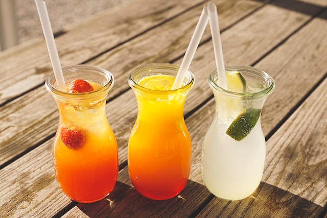 Three glass containers with straws containing what look like fruit juices