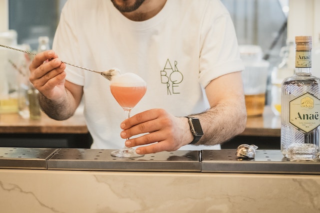 A bartender preparing a cocktail, a bottle of gin beside him