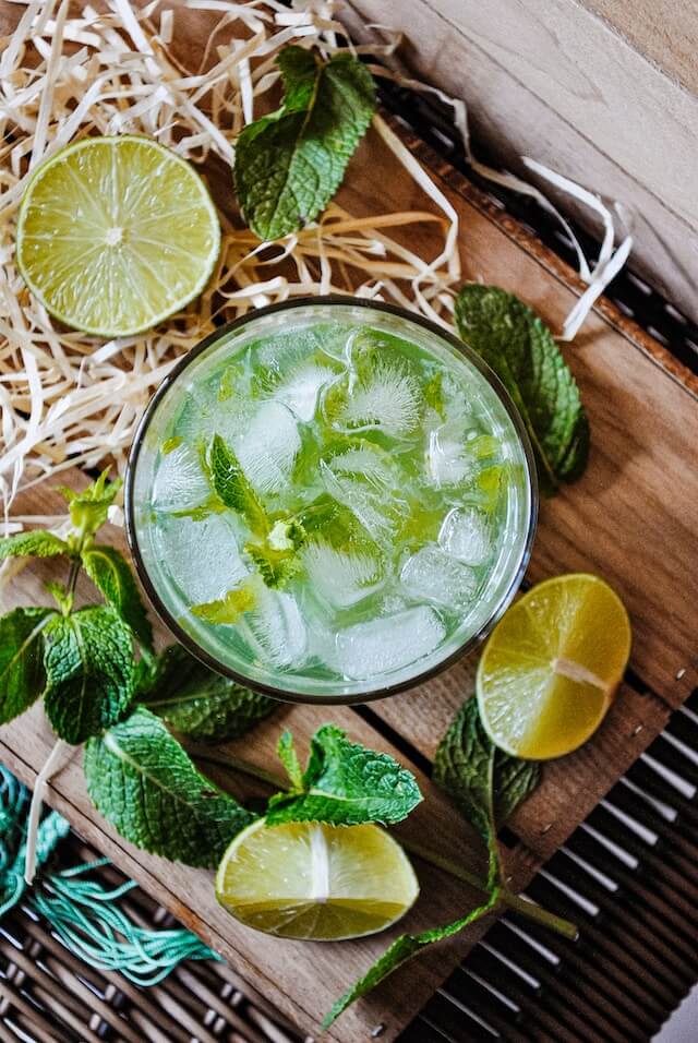 A glass filled with a greenish looking beverage, with ice cubes, and leaves of mint 