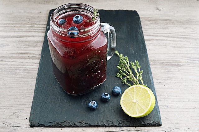 Mason glass filled with dark red liquid topped with blueberries and rosemary