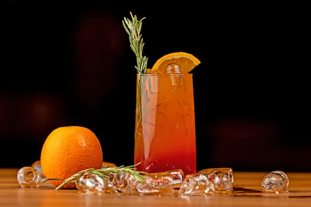 Reddish-hued drink garnished with a sprig of rosemary and a slice of orange