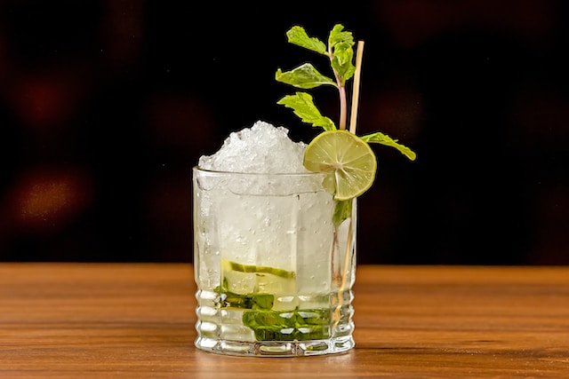 Clear liquid drink with ice garnished with lime and some herbs