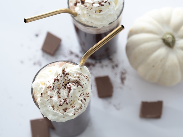 Chocolate drink topped with whipped cream beside a white pumpkin