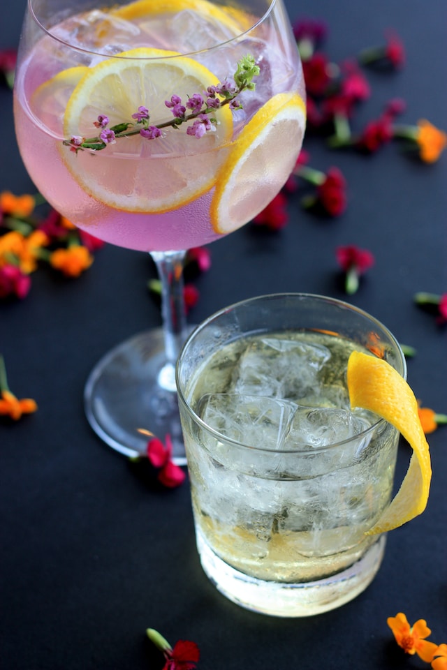 Beverages in clear glasses with citrus and floral garnish