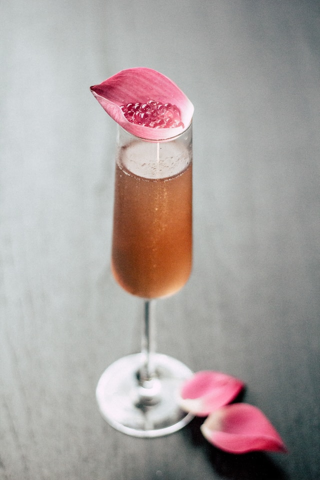 Golden beverage in a tall glass with a pink flower petal on top