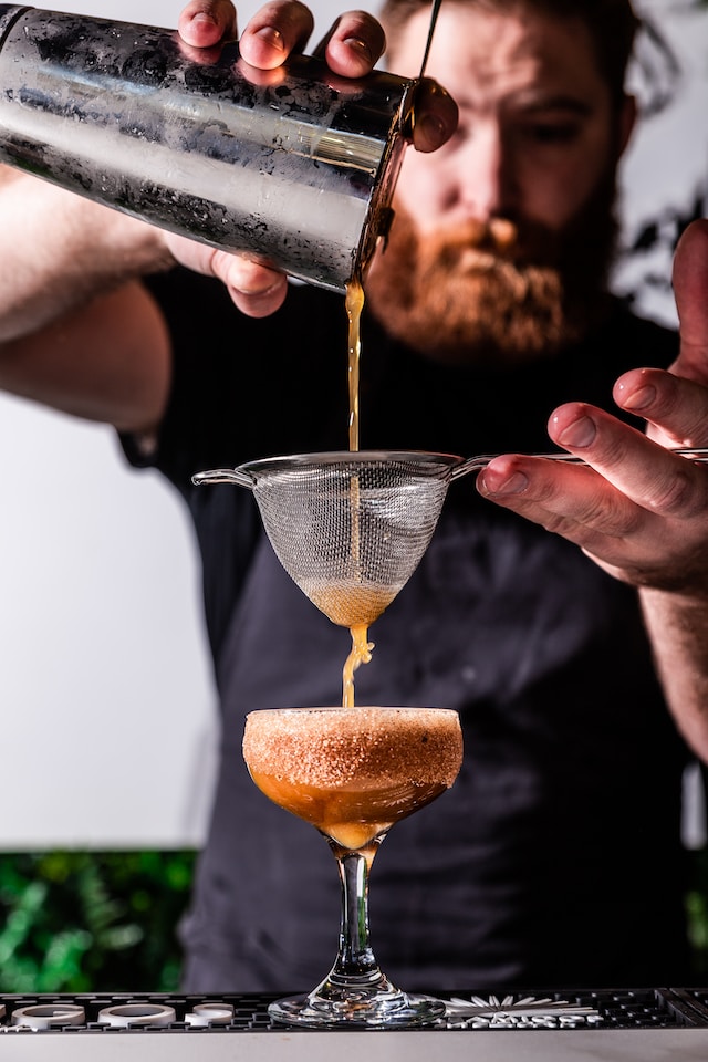 Bartender straining some orange liquid into a cocktail glass