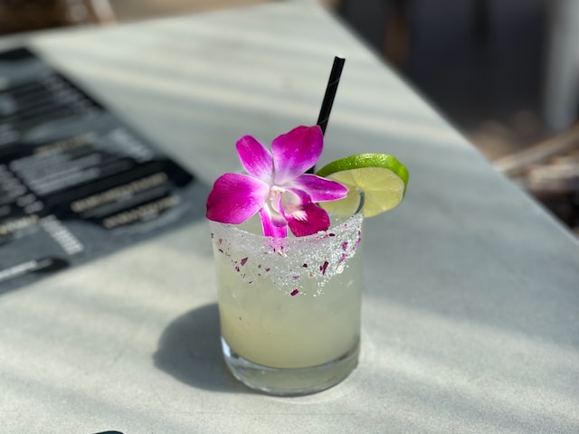Creamy looking beverage in a glass with a lime wedge and a single orchid for garnish