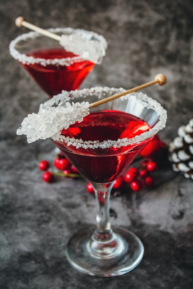 Red colored drink in a glass container garnished with sugar rim and some hard candy